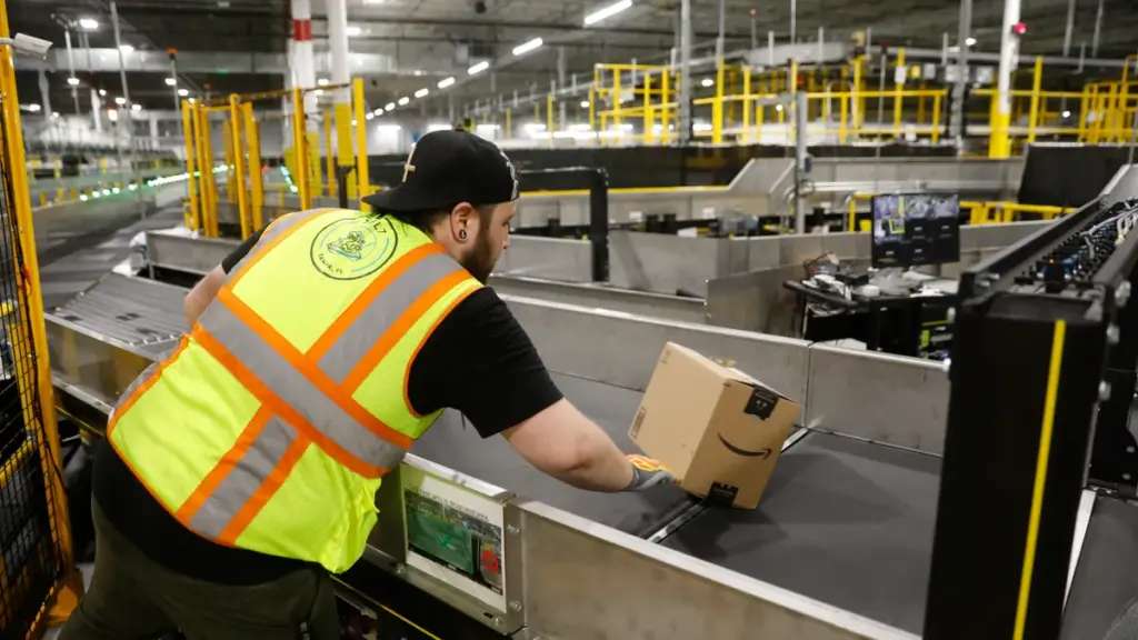 Amazon warehouse worker handling packages on a fulfillment conveyor belt.