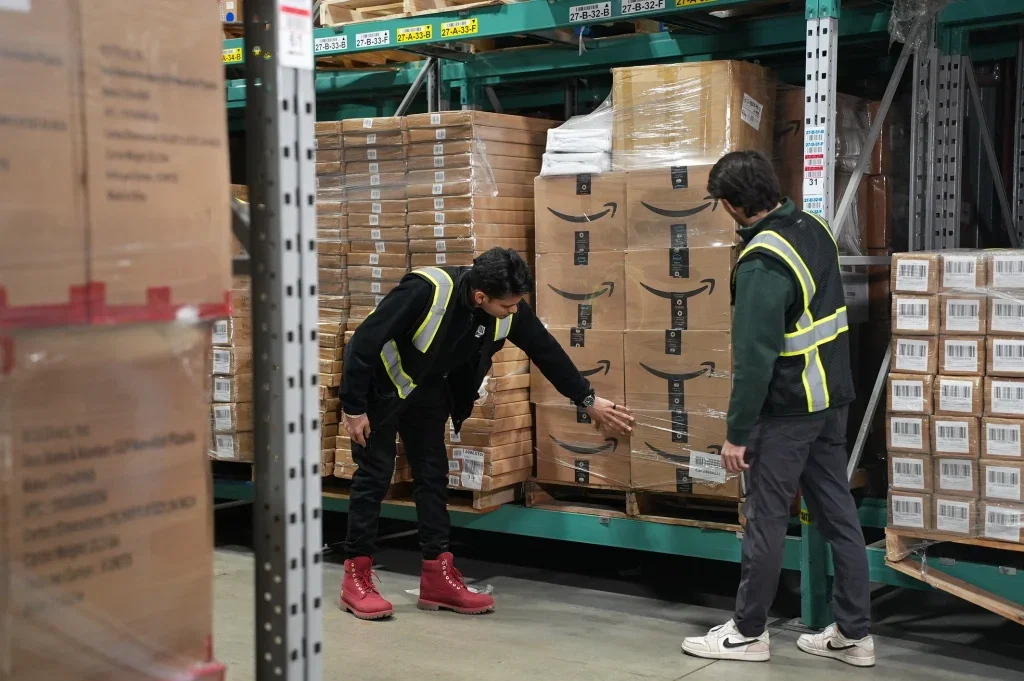 Warehouse workers inspecting Amazon shipment boxes on storage racks.