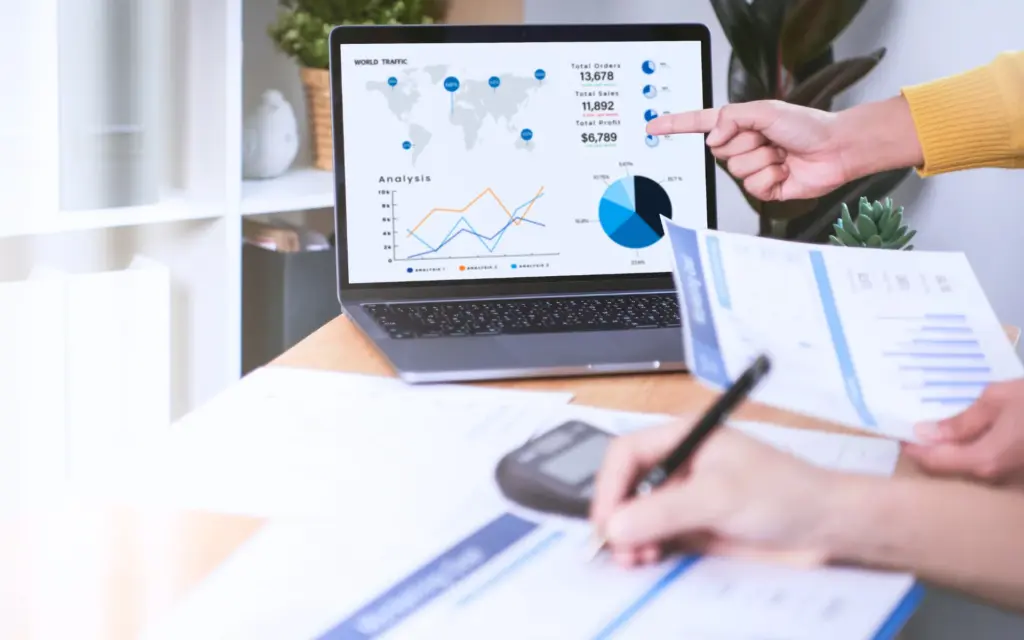 Laptop displaying sales analytics while people review reports and charts.