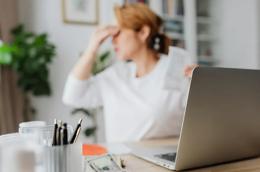 Stressed online seller sitting at a desk with a laptop while reviewing business concerns.